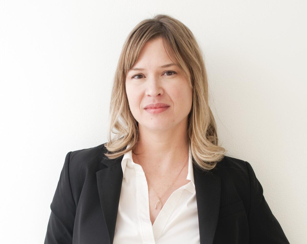 Johanna Burton stands against a white wall wearing a white shirt and black blazer