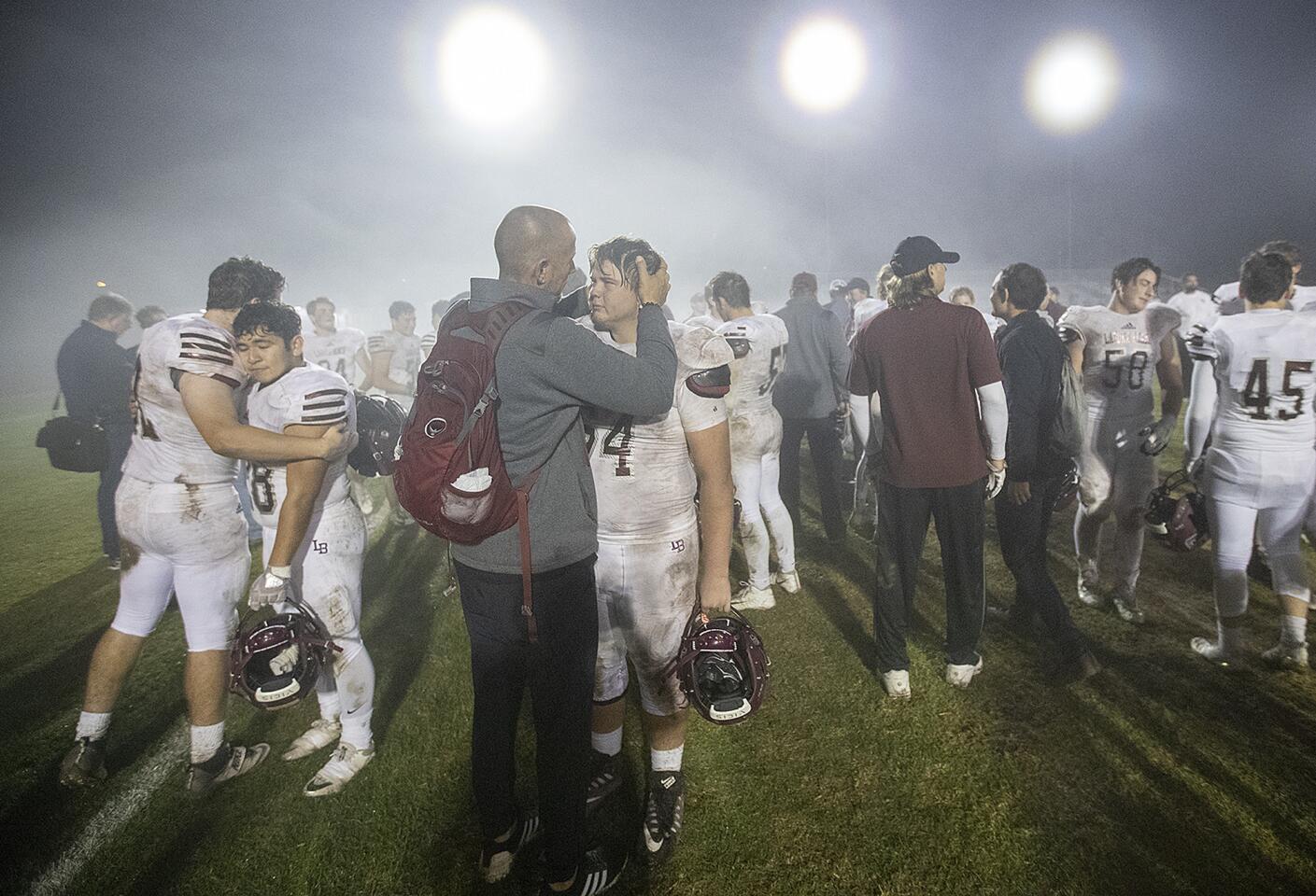 Assistant coach Darren Crawford hugs Hunter Davis following Laguna Beach High's 48-6 loss at Lakewood Artesia in a CIF Southern Section Division 12 semifinal game on Friday.