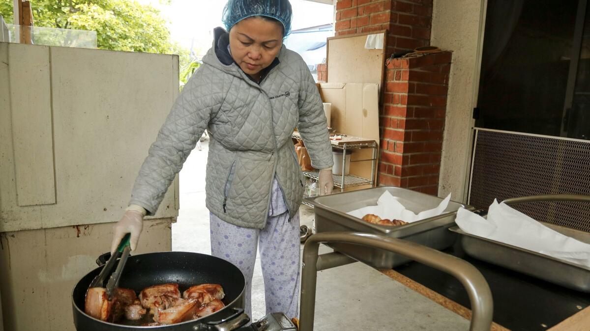 Hue Phan flips the hunks of pork in a frying pan for one of the courses she's preparing in her backyard kitchen. (Mark Boster / Los Angeles Times)