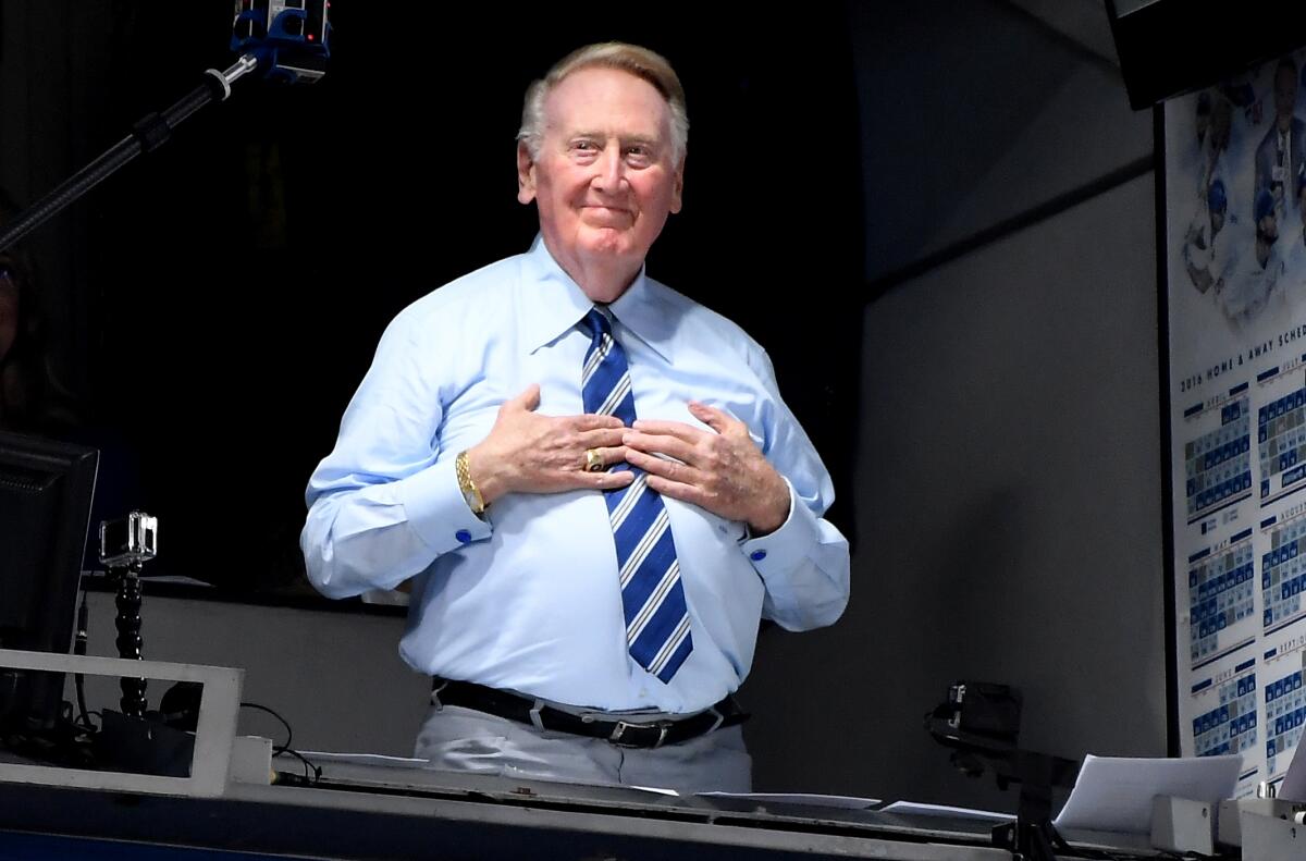 Vin Scully holds his hands to his chest looking out on the crowd while standing in the Dodger Stadium broadcast booth.