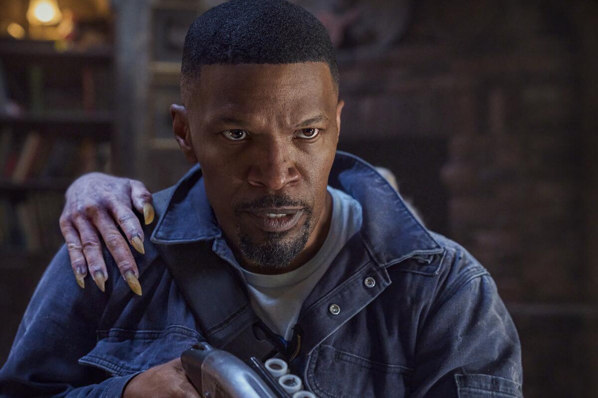 A man (Jamie Foxx) with a shotgun intensely hunts vampires - as a ghoulish hand creeps onto his shoulder from behind.