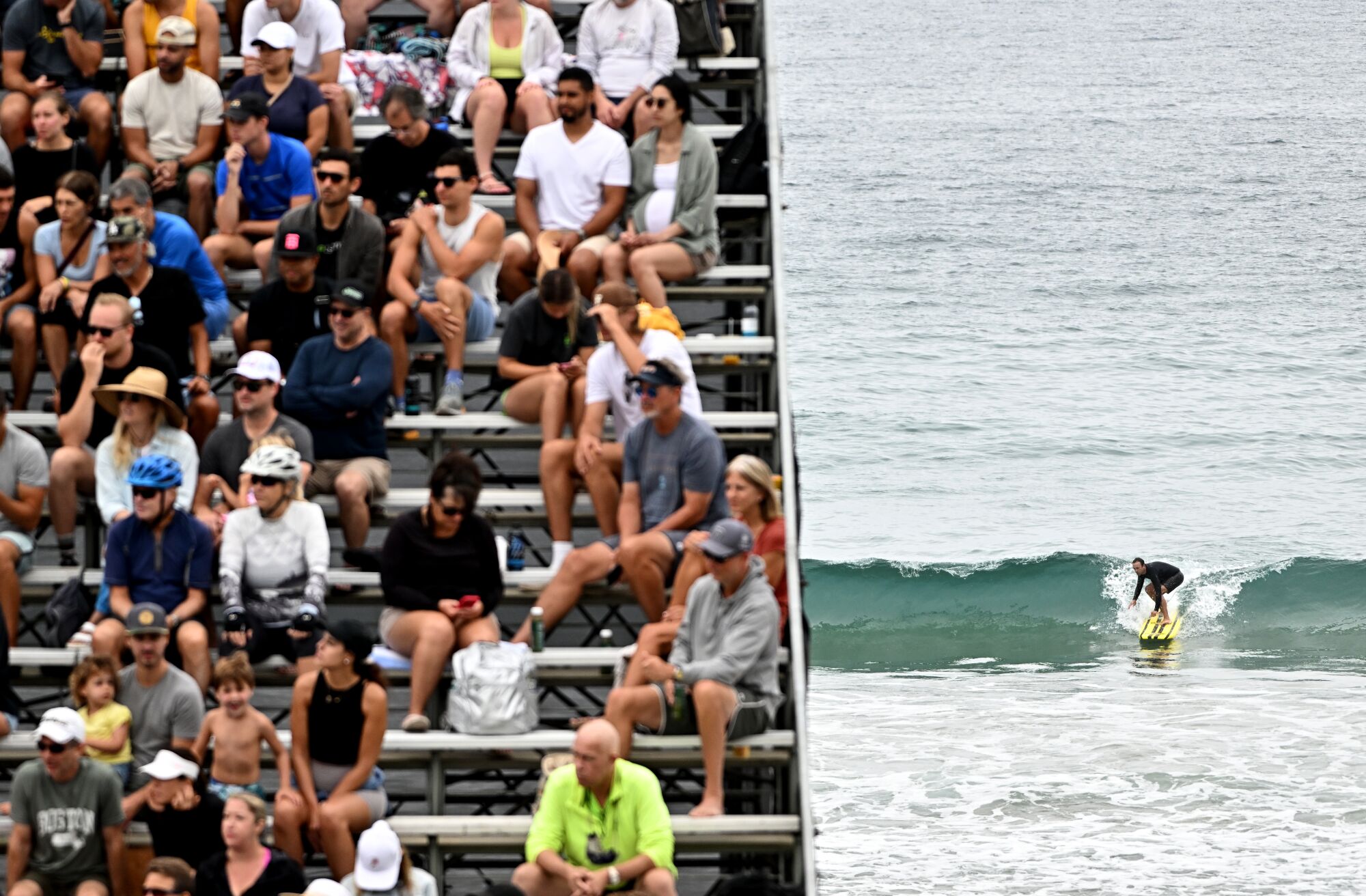 A surfer rides a wave as the crowd watches the AVP Manhattan Beach Open.