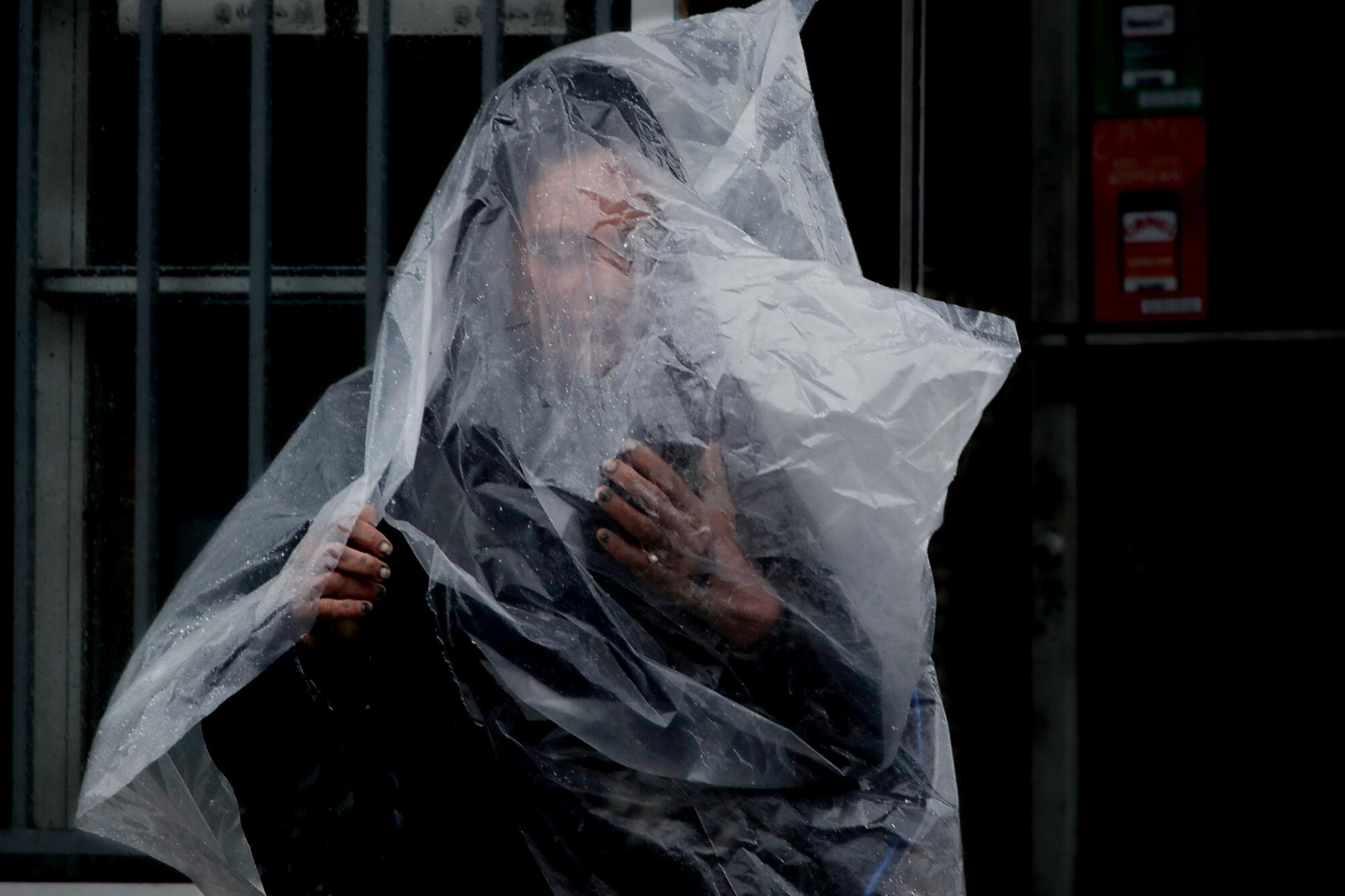 A woman uses a plastic sheet to shelter from the rain Monday in Long Beach.
