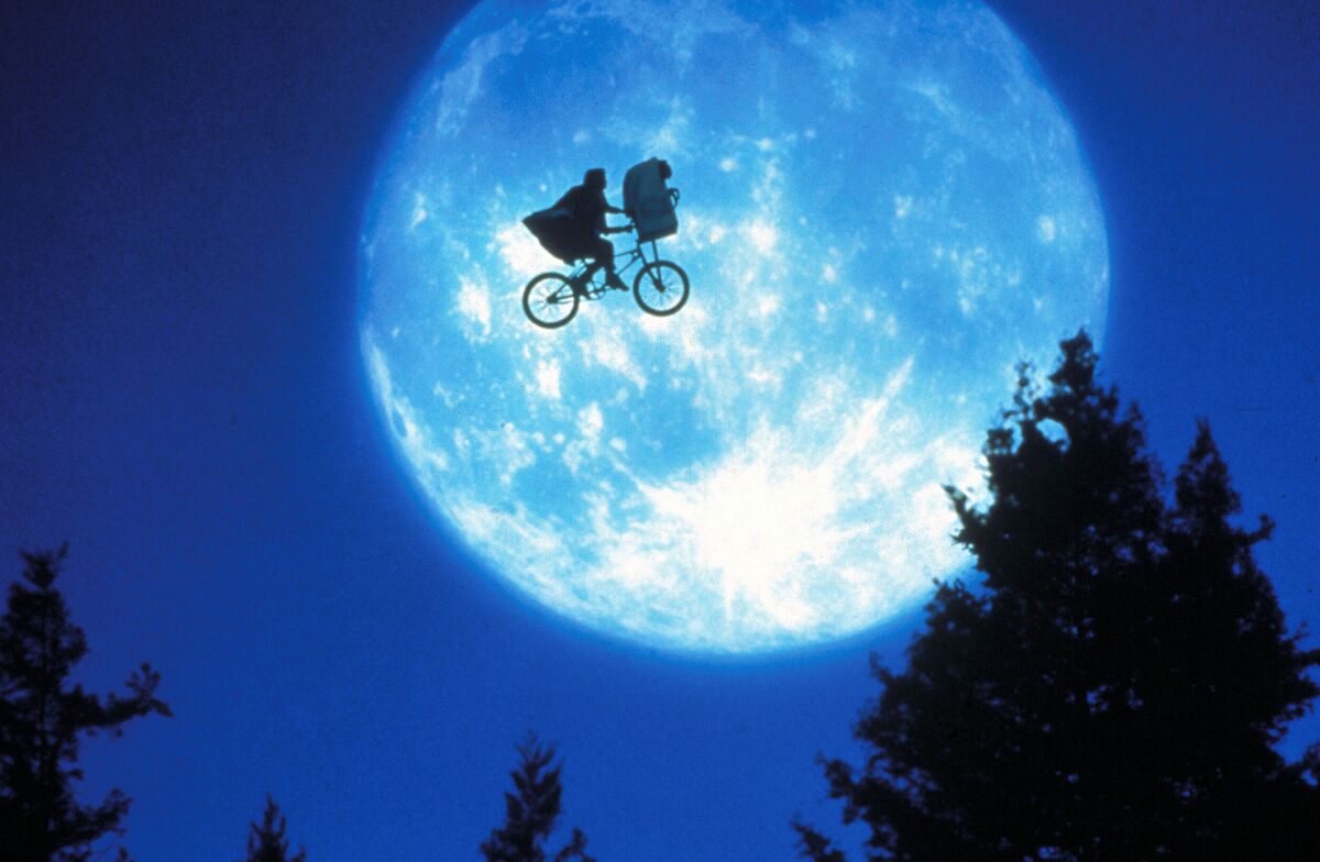 A boy on a bike with an alien in his basket, silhouetted against the moon in the 1982 movie "E.T. the Extra-Terrestrial."