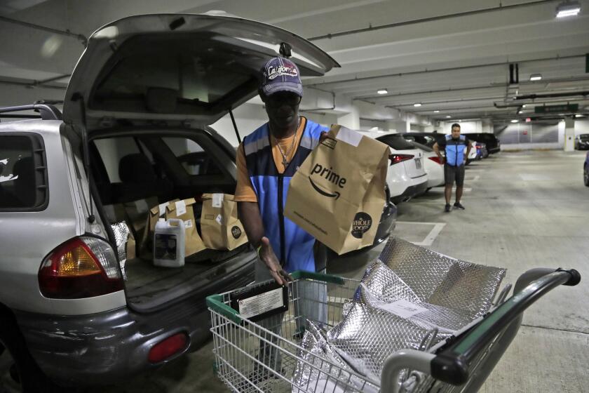 FILE - In this March 31, 2020, file photo, Samuel Diaz, a delivery worker for Amazon Prime, loads his vehicle with groceries from Whole Foods, in Miami, during the COVID-19 pandemic. A leap in U.S. unemployment has thrown a spotlight on one type of work still in high demand during the coronavirus pandemic: Gig work delivering groceries, meals and packages. (AP Photo/Lynne Sladky, File)