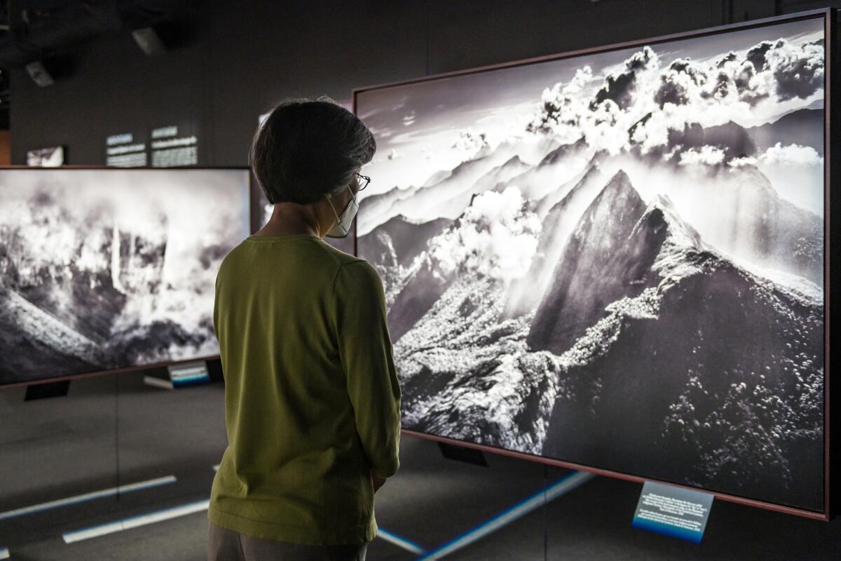 A woman stands in a gallery viewing a large black-and-white photo of clouds and mountains