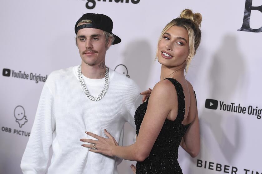 Justin Bieber, dressed in white long sleeve and Hailey Bieber in black dress smiling together on red carpet