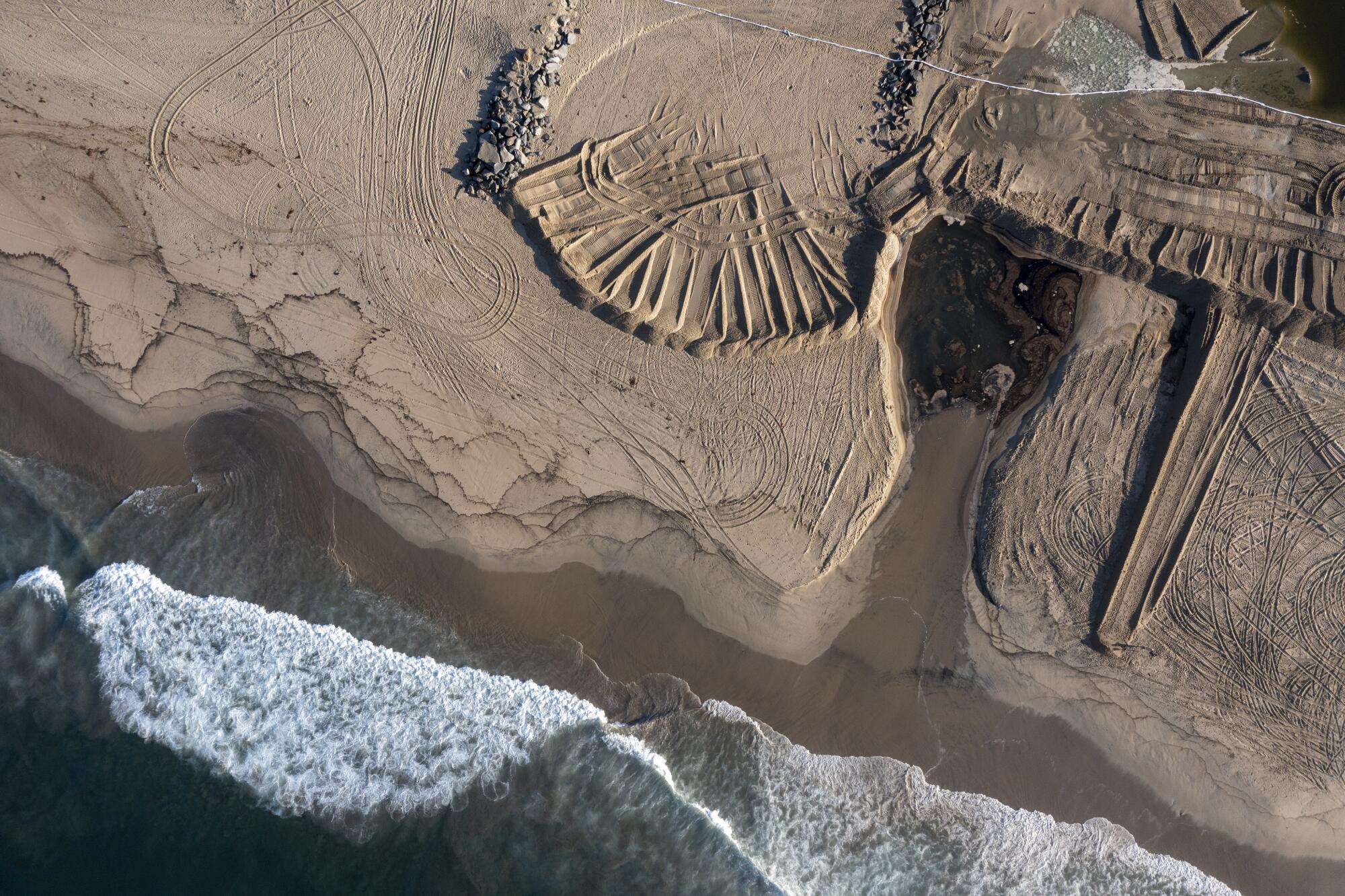 Waves break along a sandy stretch with a dark brown patch on the right