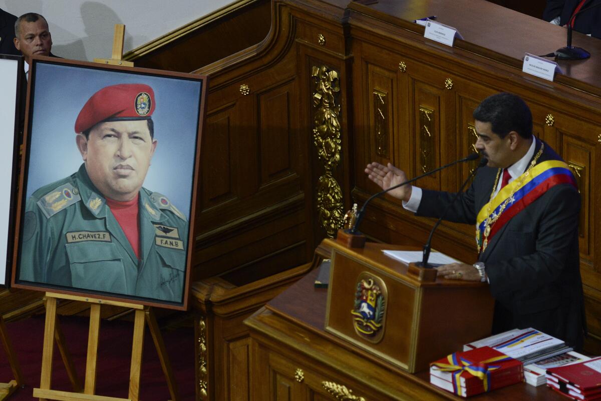 A portrait of a man in a red beret and green uniform is displayed next to a man in a suit and a sash speaking at a lectern