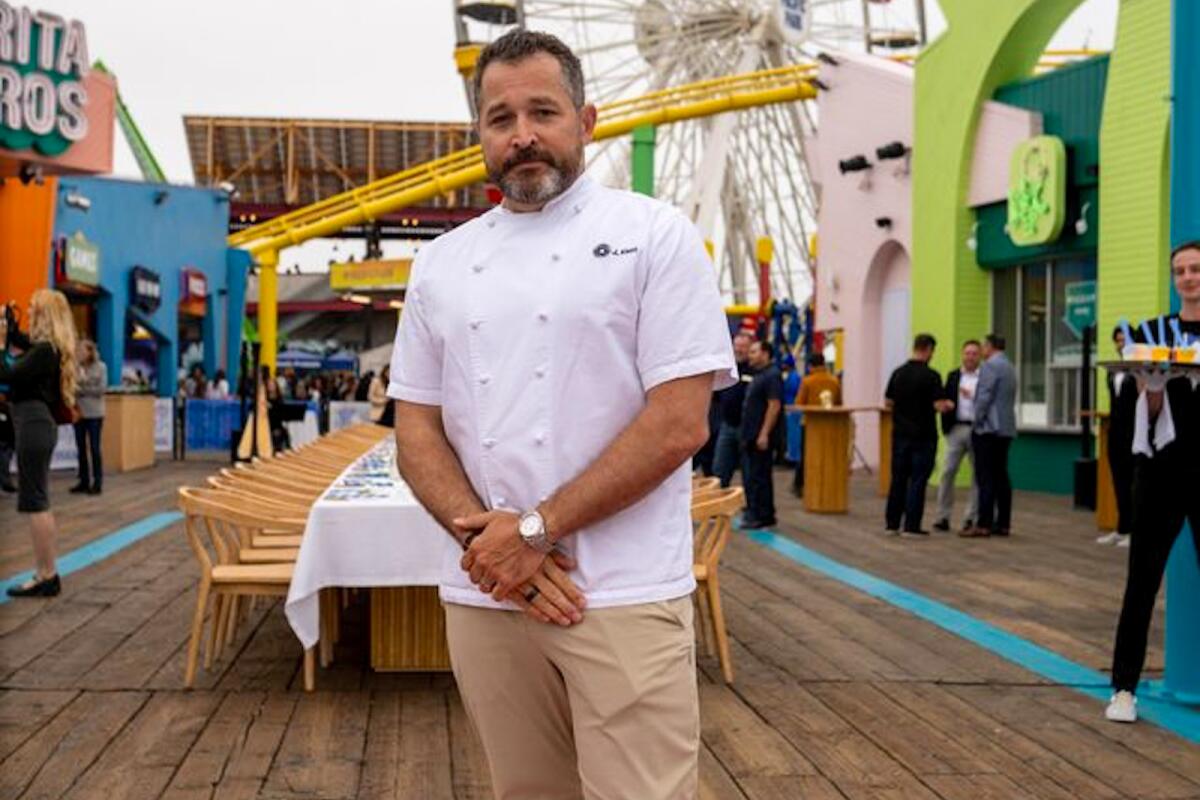 James Kent stands on the Santa Monica Pier, restaurants and rides behind him