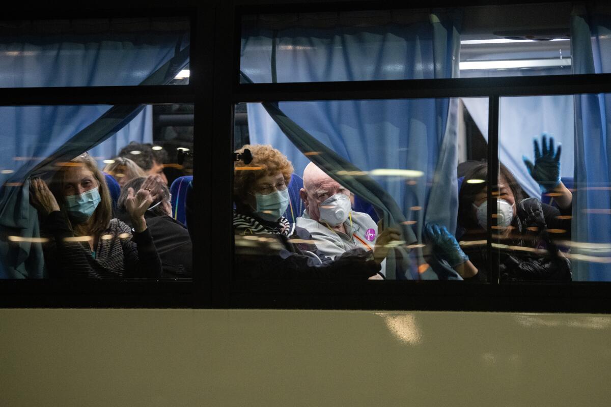 American citizens wave from a bus as they leave the quarantined Diamond Princess cruise ship in Yokohoma, Japan, en route back to the U.S.
