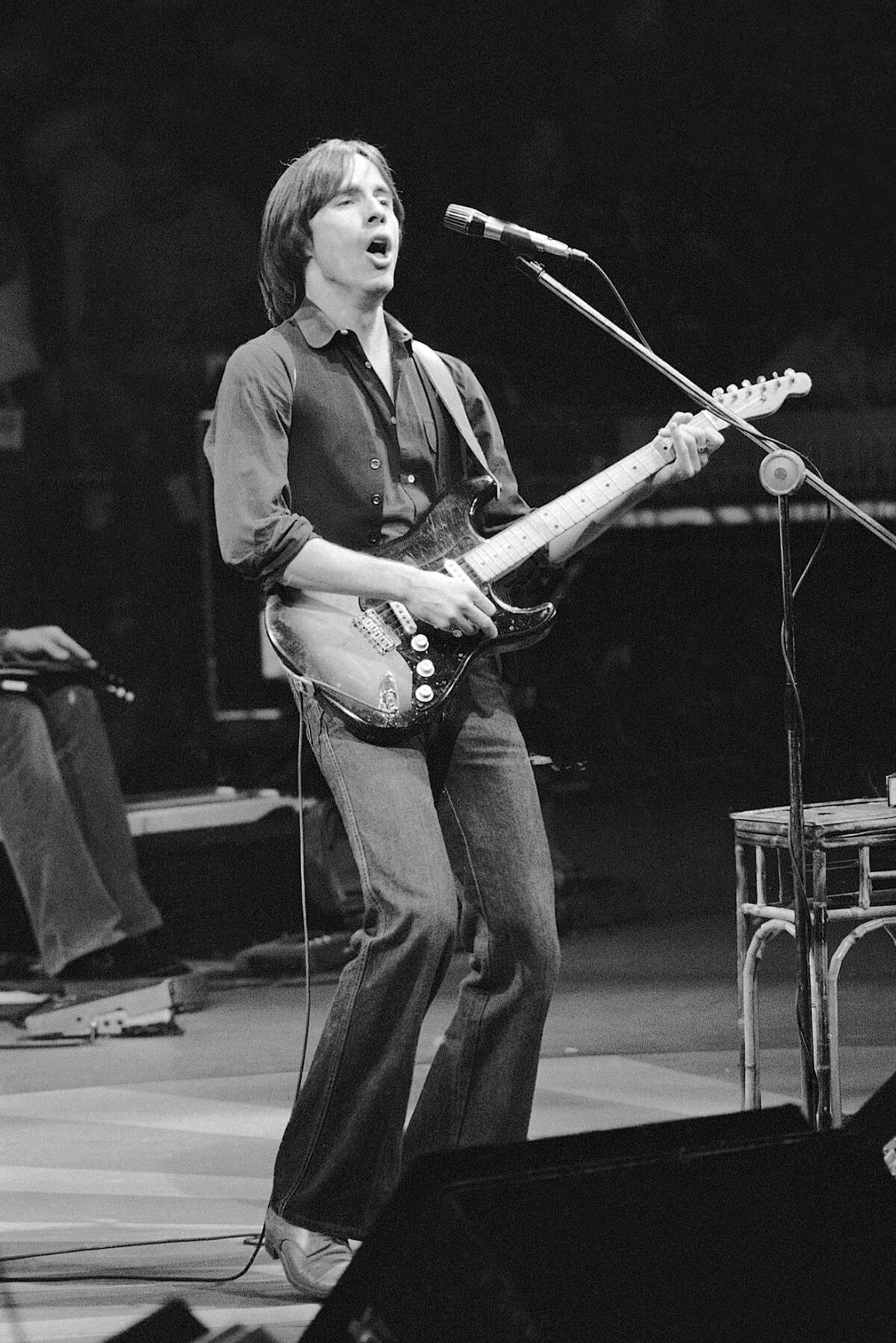 A young man plays the guitar and sings onstage