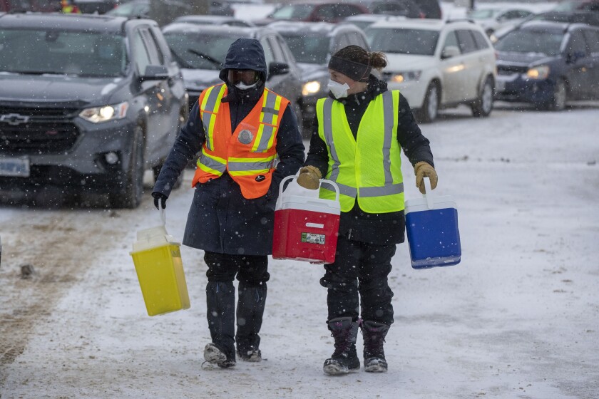 Clinic volunteers walk with coolers of syringes during a drive through COVID-19 vaccine clinic at St. Lawrence College in Kingston, Ontario, on Sunday Jan. 2, 2022. (Lars Hagberg /The Canadian Press via AP)