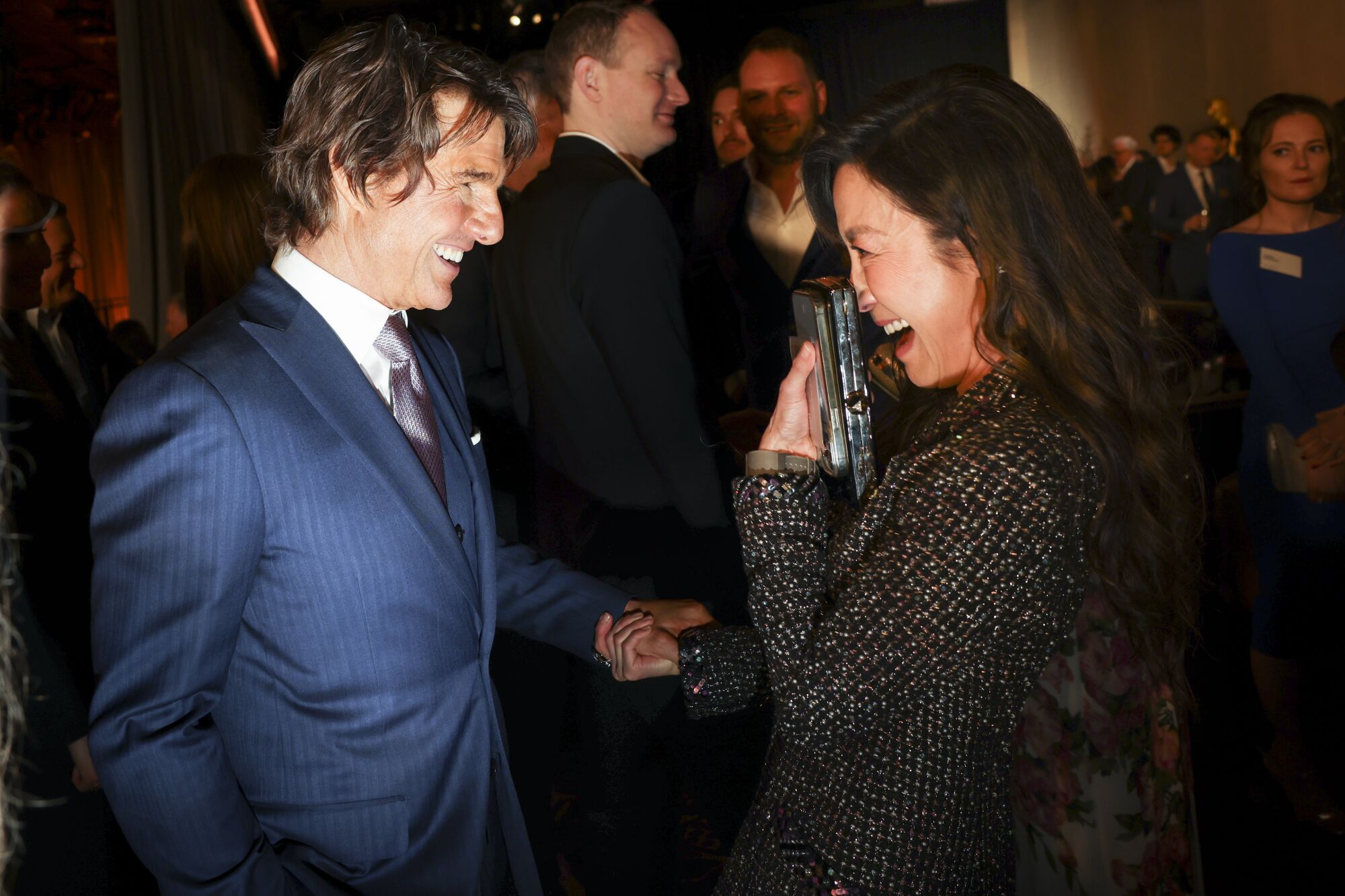 Actors Tom Cruise and Michelle Yeoh laugh as they fact each other in a crowd.