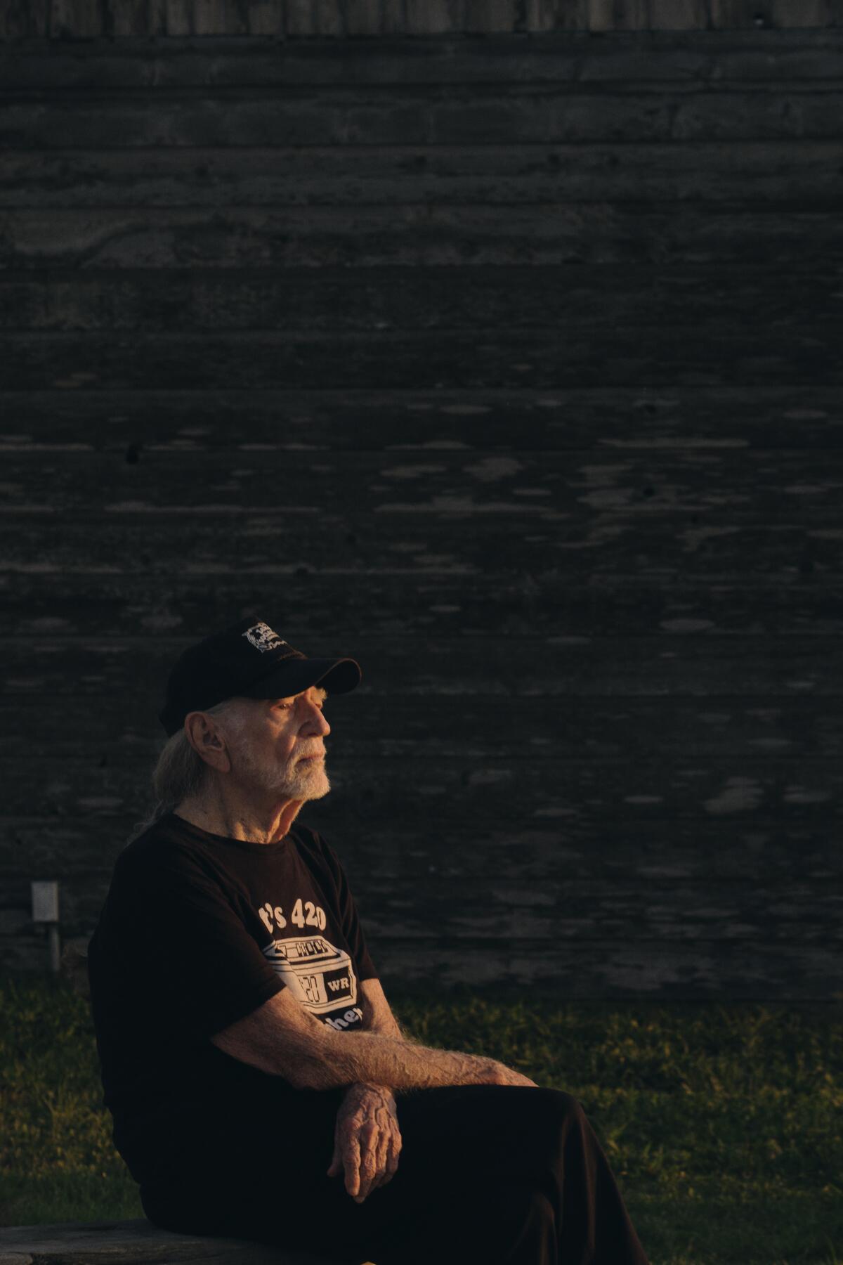 Willie Nelson sitting outside in a T-shirt against a dark background