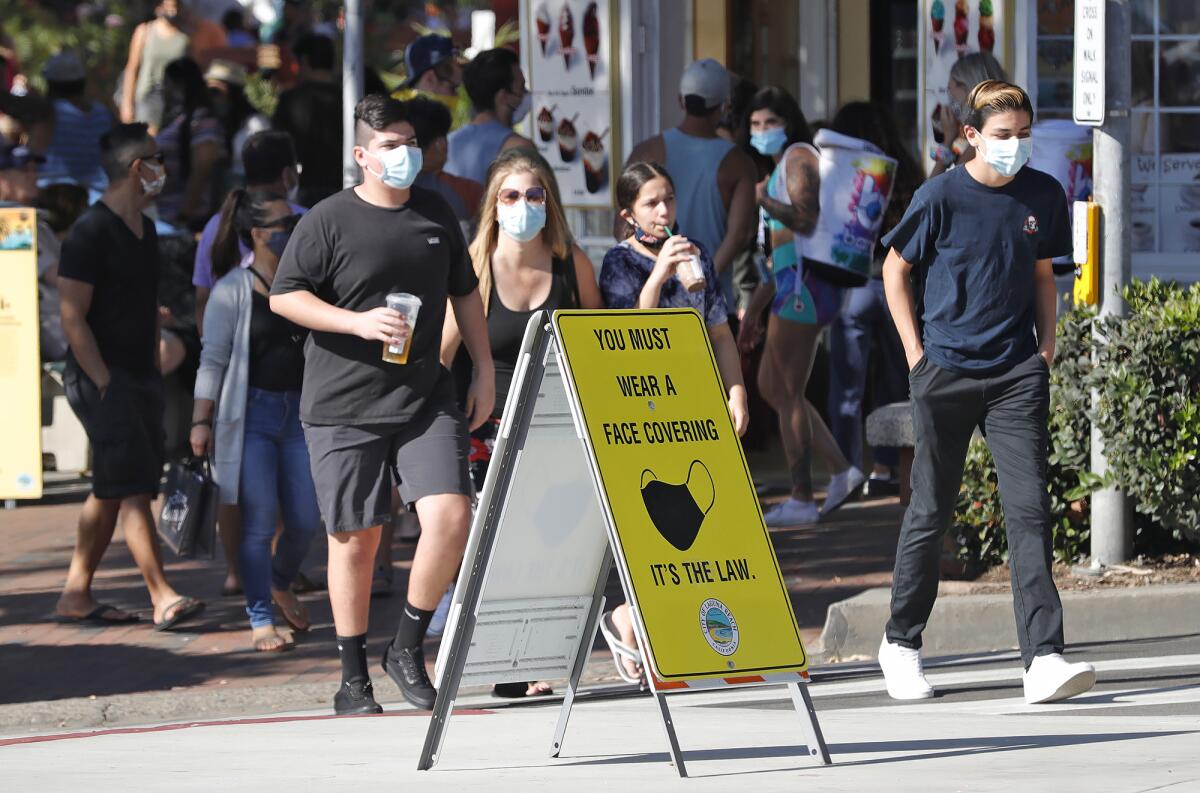 A mask-wearing group crosses the street as they walk along the sidewalks in Laguna Beach on Aug. 31.