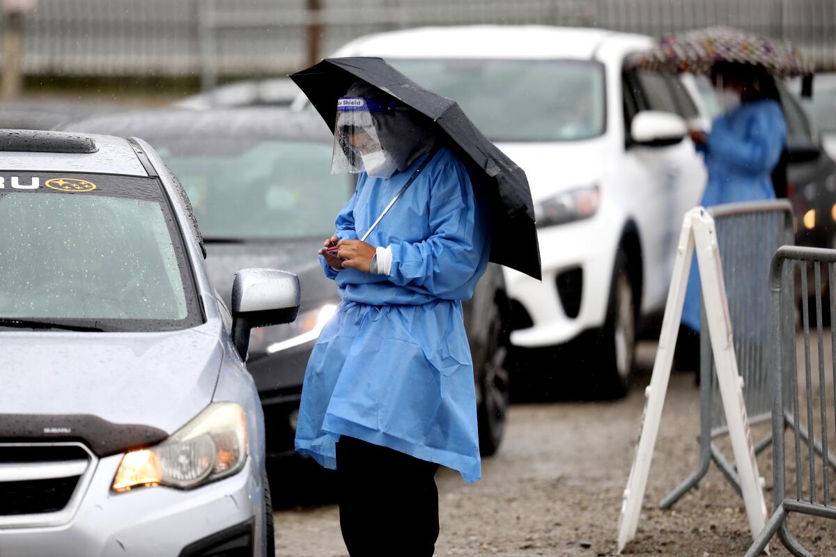 A healthcare professional stands under an umbrella at a drive-through coronavirus testing site.