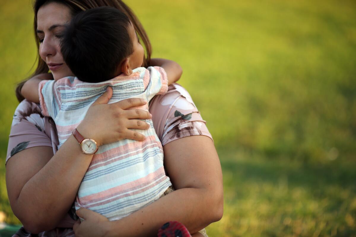 A woman hugs a young her child in a park.