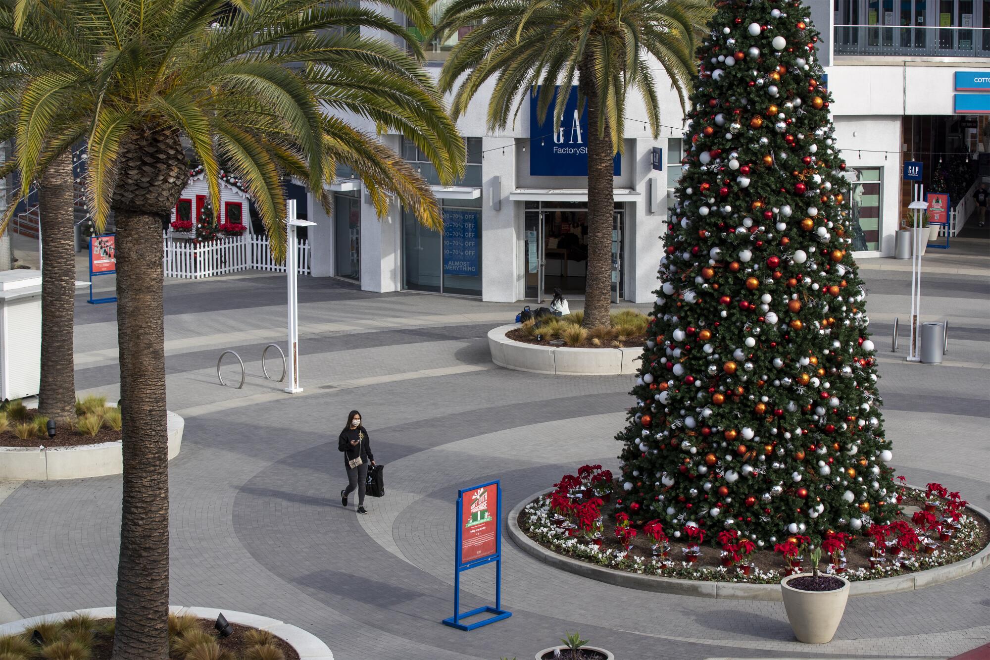 A woman wearing a mask walks through a mostly empty shopping mall at The Pike Outlets in Long Beach.