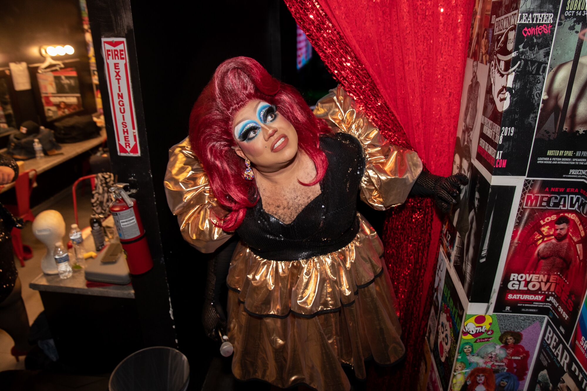 A drag queen in black and gold, red wig and plentiful blue eye makeup looks up