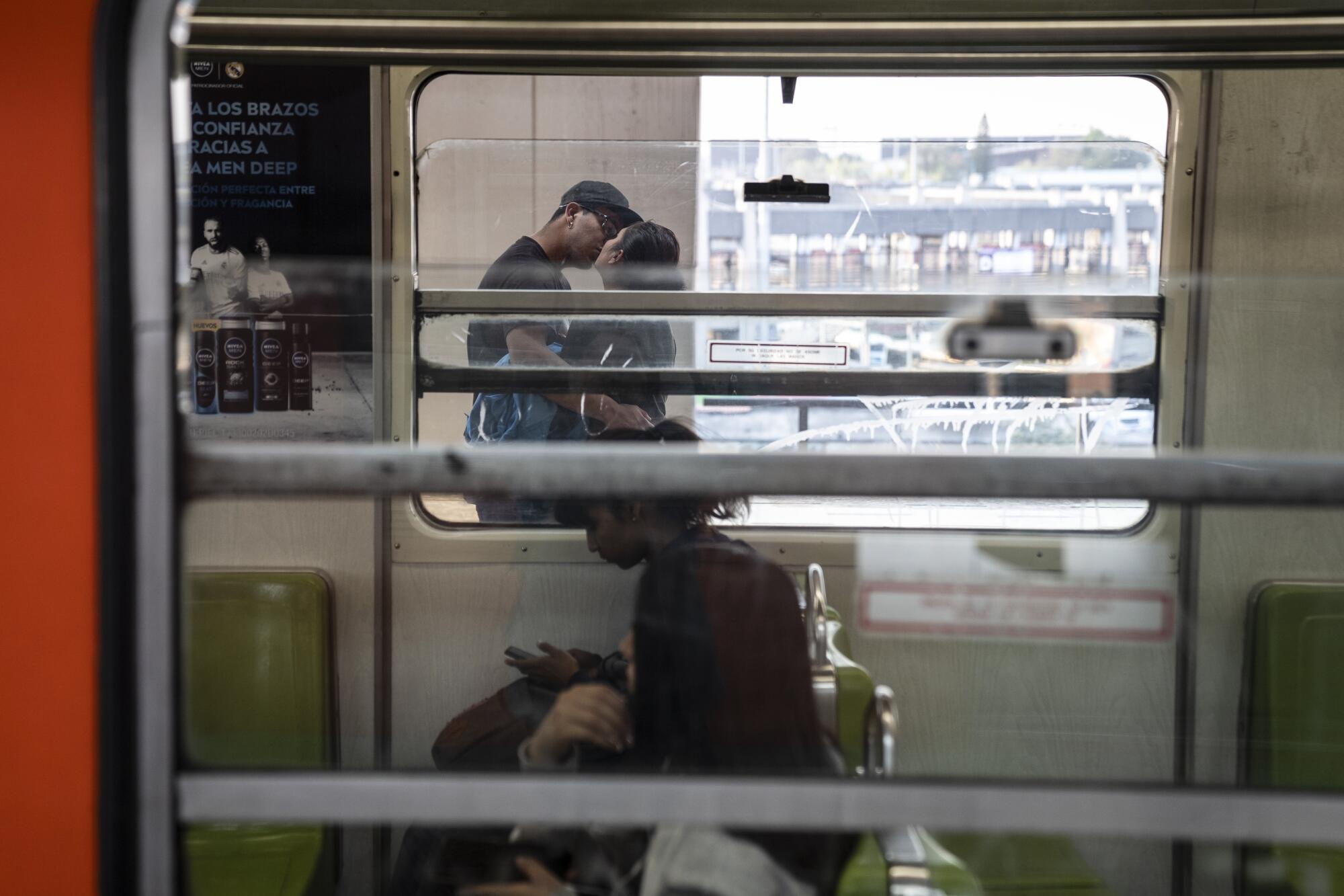 A couple kiss as seen through the windows of a subway car.