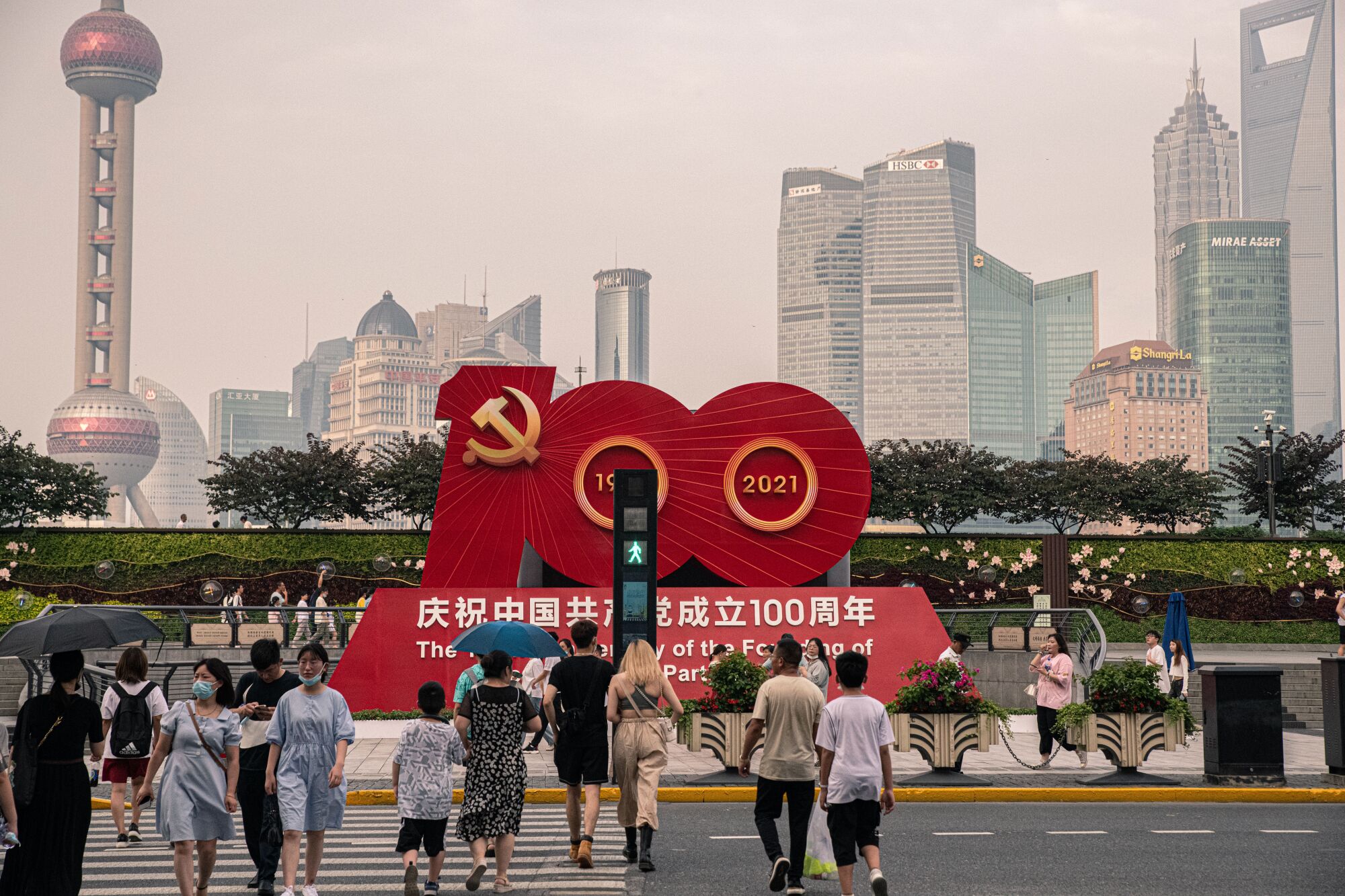 A sign in red depicting the number 100 and Chinese characters sits near a road with pedestrians