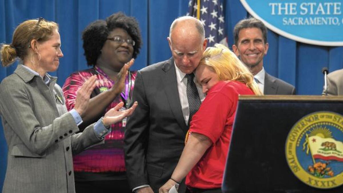 Gov. Jerry Brown hugs Burger King worker Holly Dias at a news conference on the minimum wage legislation. She’s worked for minimum wage for nine years.