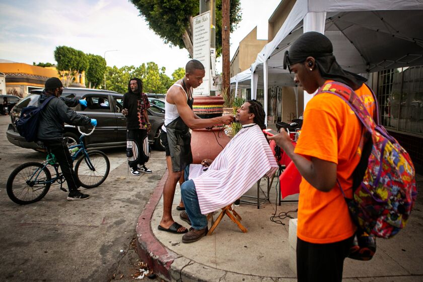 LEIMERT PARK, CA - JUNE 15: Jacket Rashad, a street barber, gives Rashad Karim, a food vendor, a haircut on Degnan Blvd. on Tuesday, June 15, 2021 in Leimert Park, CA. The Leimert Park community is excited for the reopening and is preparing for a huge Juneteenth block party. (Jason Armond / Los Angeles Times)