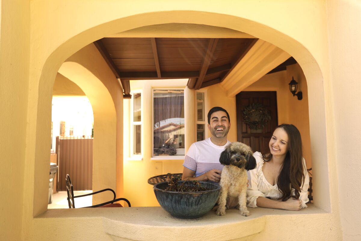 A man and woman pose with their small dog on the porch of their home.