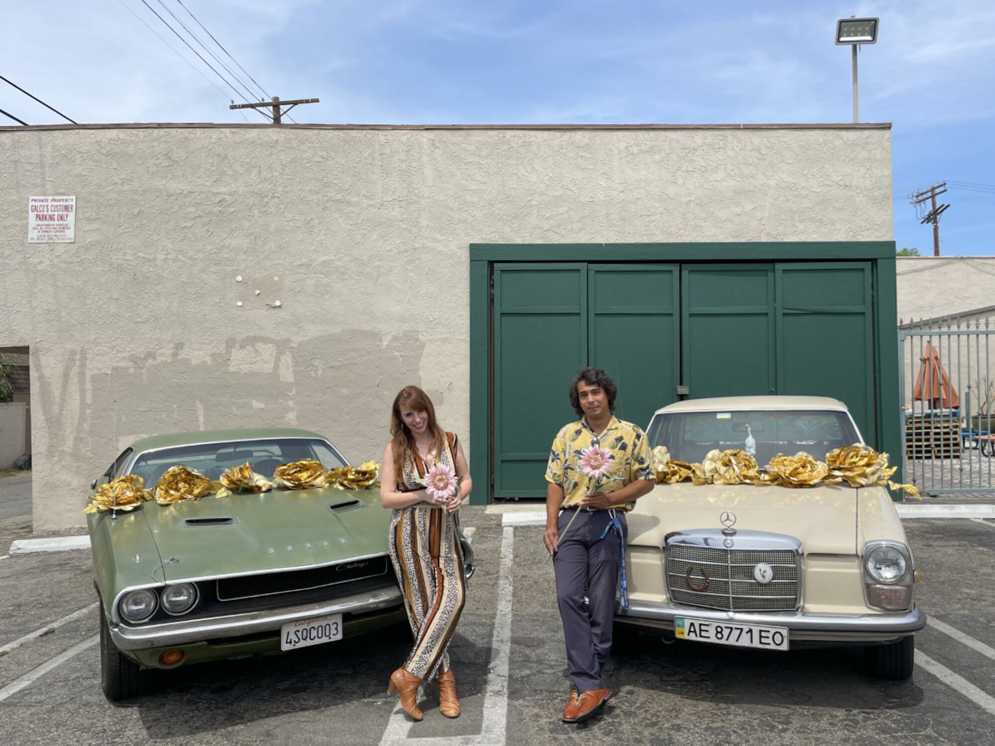 Two people pose in front of their vintage cars.