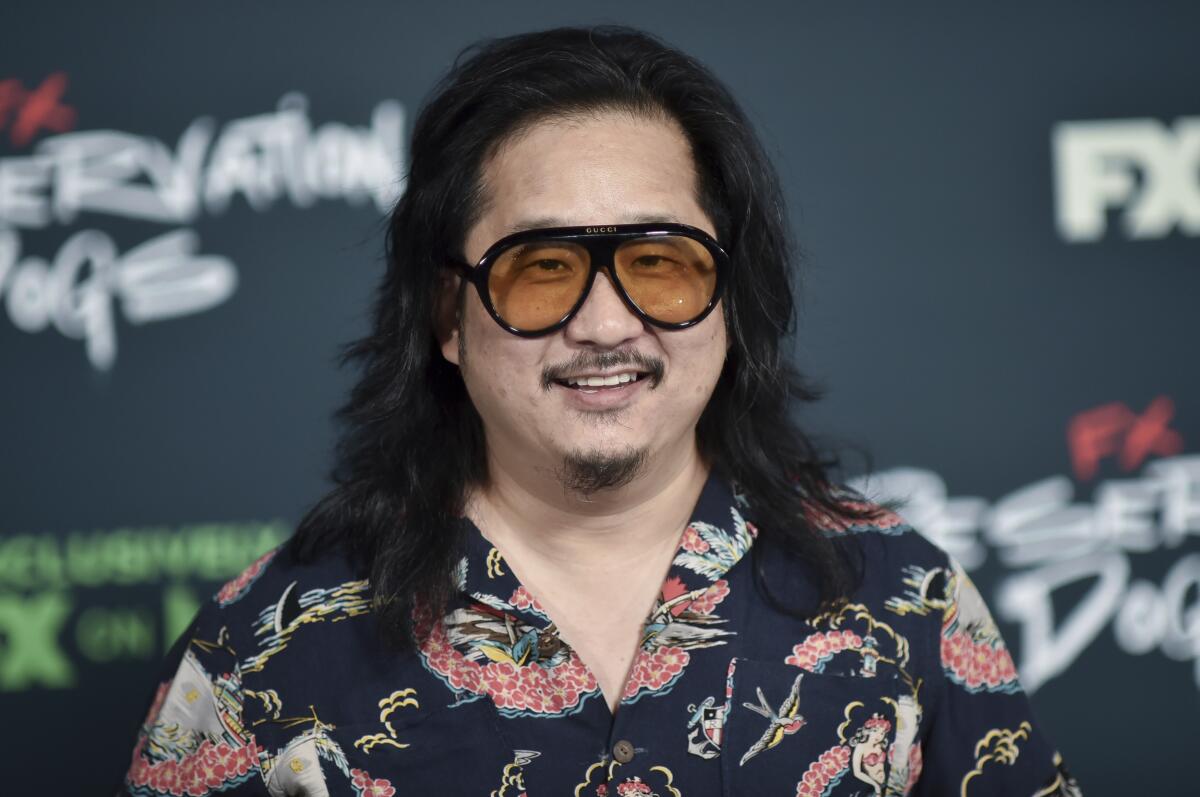 Bobby Lee smiles while wearing large sunglasses and a printed shirt.