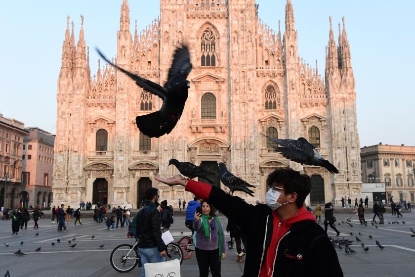 A man wearing a protective facemask plays with pigeons in the Piazza del Duomo in central Milan, on February 24, 2020 following security measures taken in northern Italy against the COVID-19 the novel coronavirus. - Italy reported on February 24, 2020, its fourth death from the new coronavirus, an 84-year old man in the northern Lombardy region, as the number of people contracting the virus continued to mount. (Photo by Miguel MEDINA / AFP) (Photo by MIGUEL MEDINA/AFP via Getty Images)