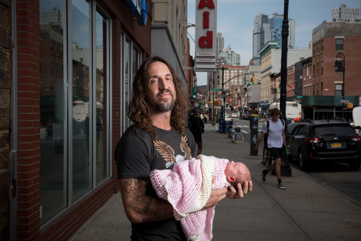 Joseph Arthur poses for a portrait on a city sidewalk holding his 4-day-old daughter. 