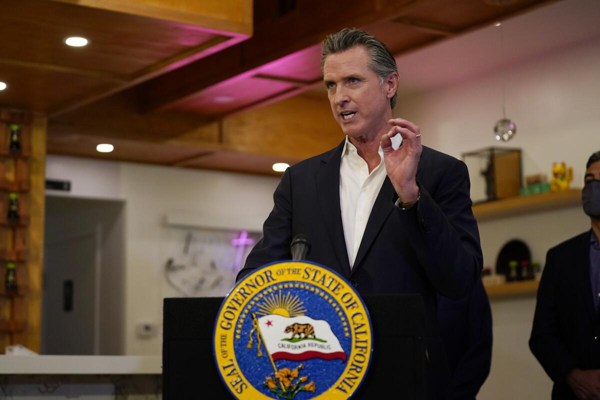 Gavin Newsom gestures with his left hand while speaking at a lectern with the seal of the governor of California on it