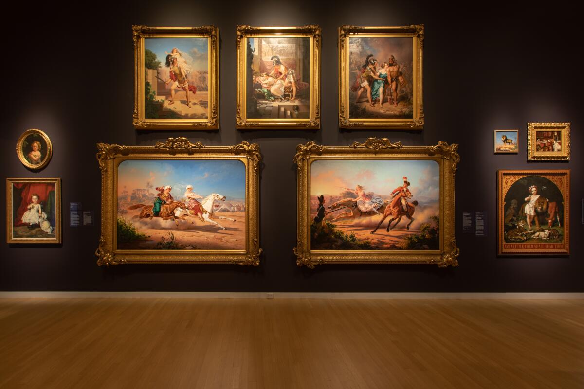 Paintings hang in a group on a dark wall in the Crocker Art Museum
