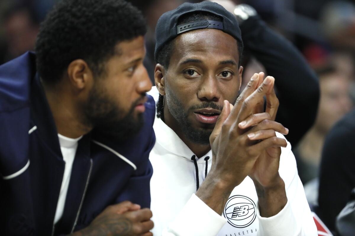 Injured Clippers stars Paul George, left, and Kawhi Leonard watch a game from the bench in street clothes.