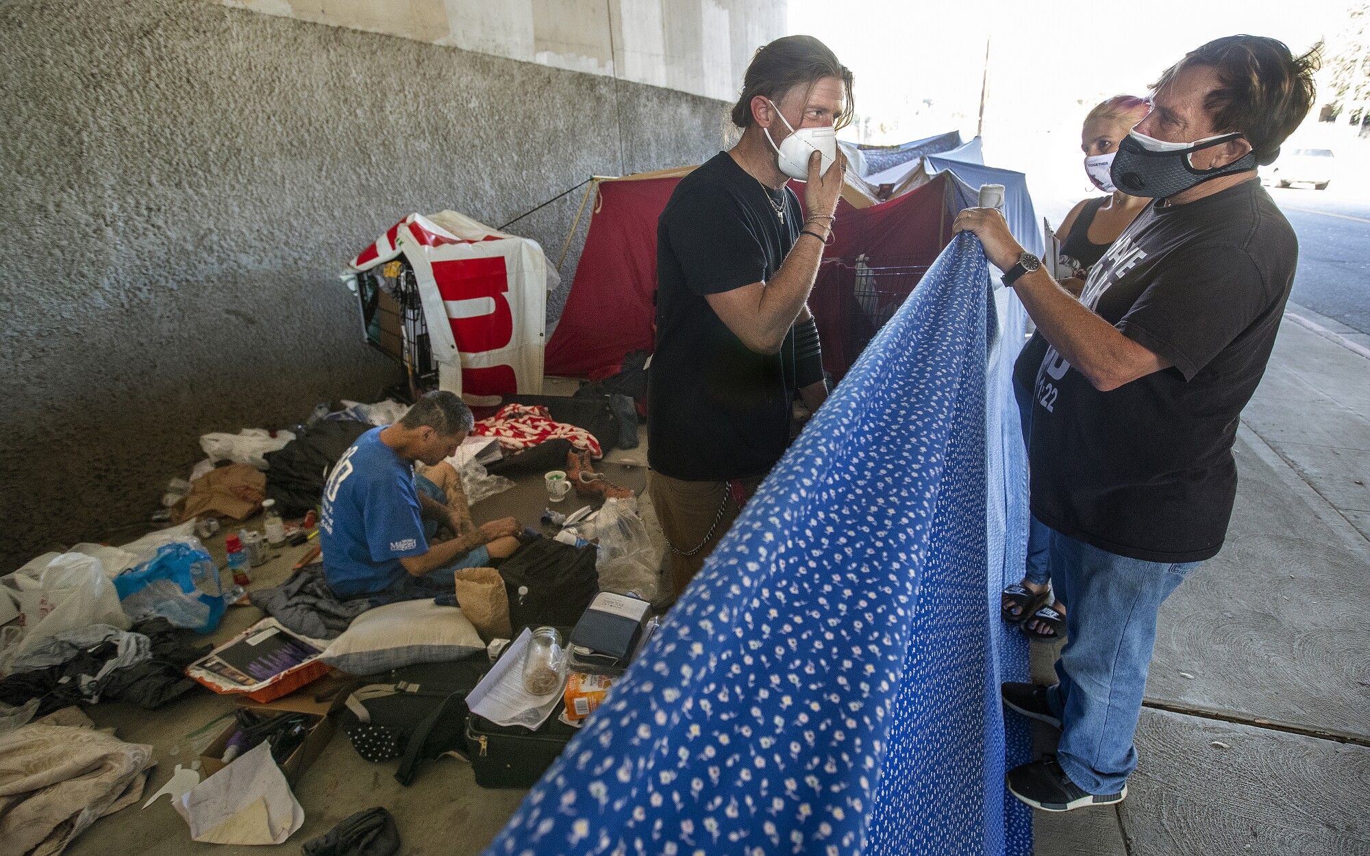 A pastor and an activist talk to a homeless person under a freeway.