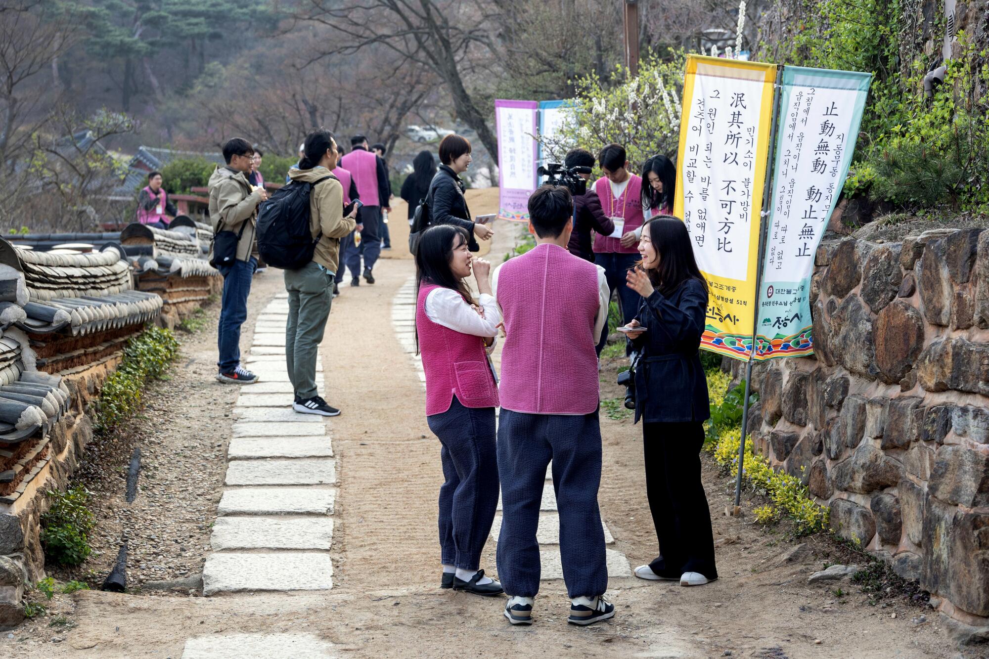 People stand talking near a stone wall and banners in an outdoor setting