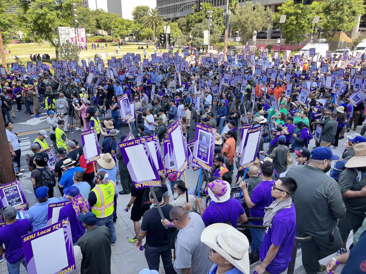 A crowd of people holding signs, many wearing purple shirts.