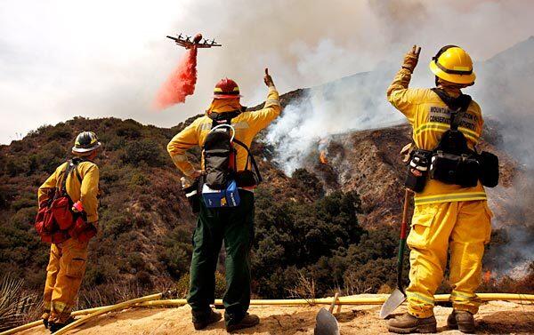 Firefighters, from left, Steven Moak, Ken Nelson and Gil Alvarex with the Mountain Recreation Conservation Authority watch as a plane drops fire retardant off Angeles Crest Highway.