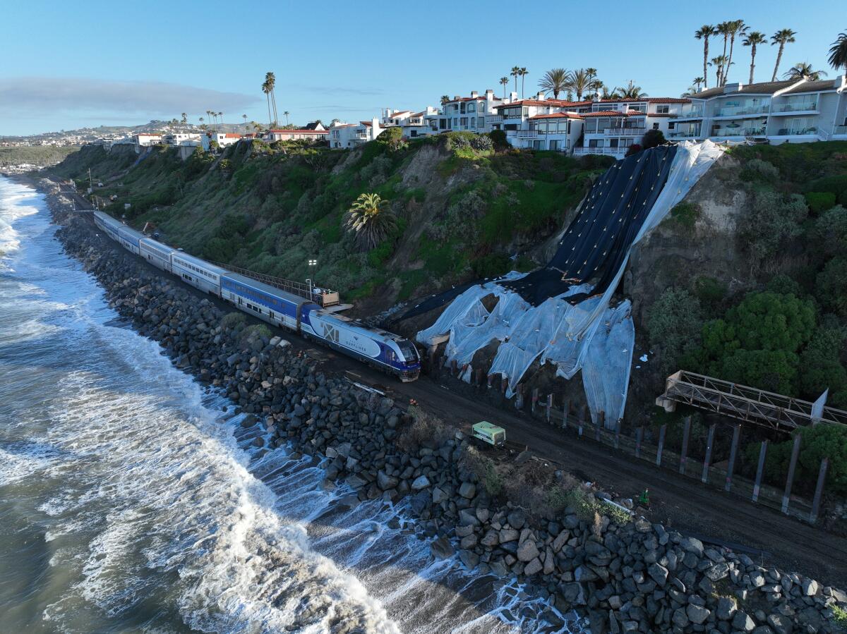 A train passes by a cliff next to an ocean.