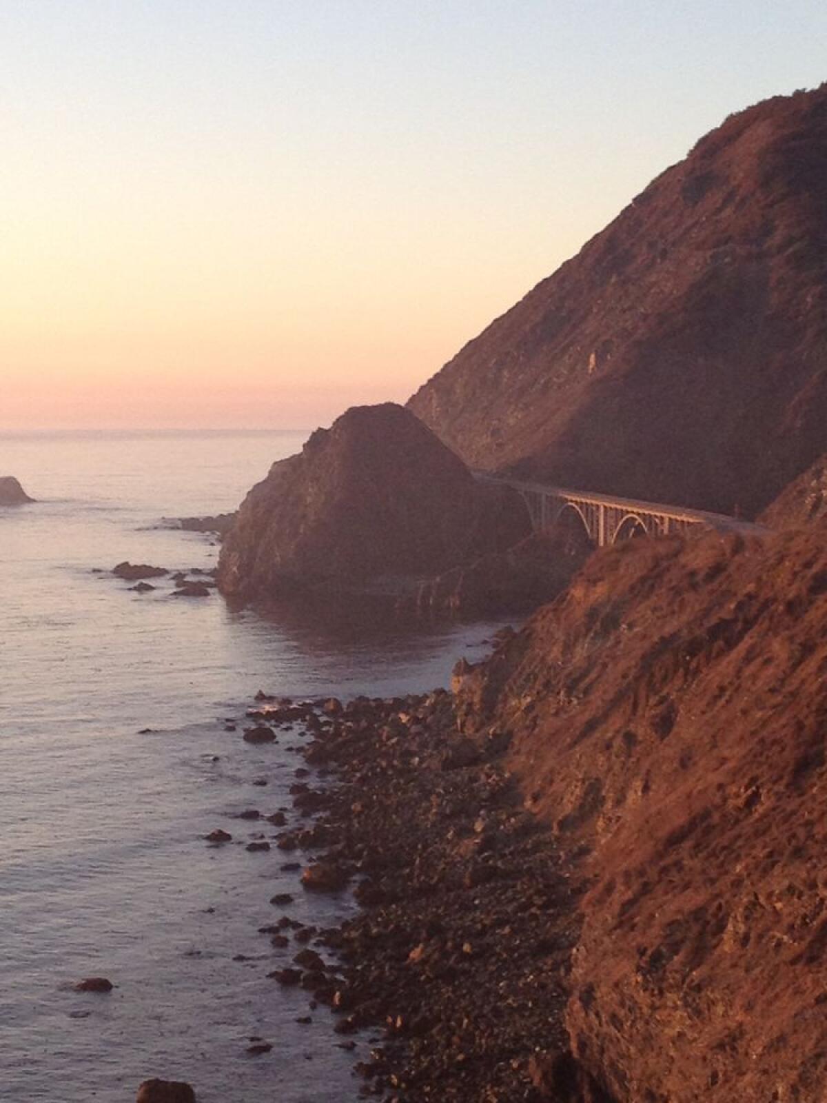 A bridge spans the ocean-facing gap between two steep mountains.