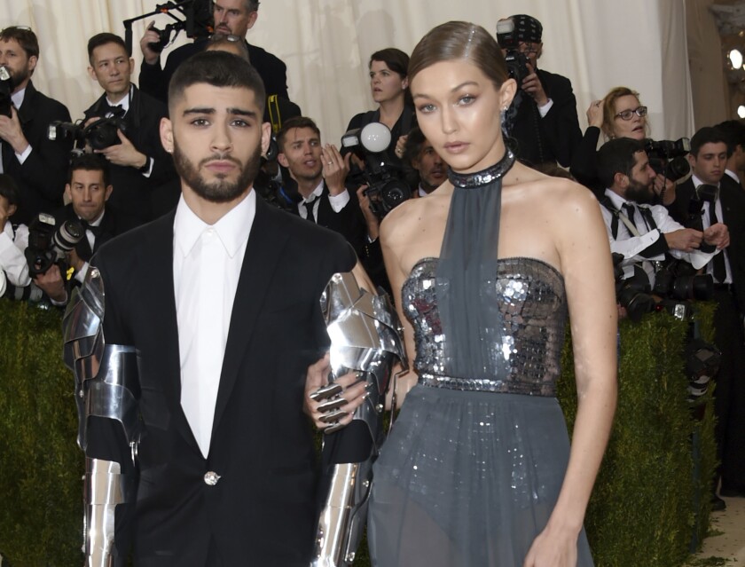A man in a dark suit with metallic arms poses with a woman in a metallic dress