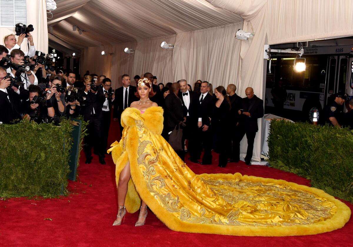 Rihanna poses on the red carpet in a yellow embroidered, fur-trimmed gown with a long train.