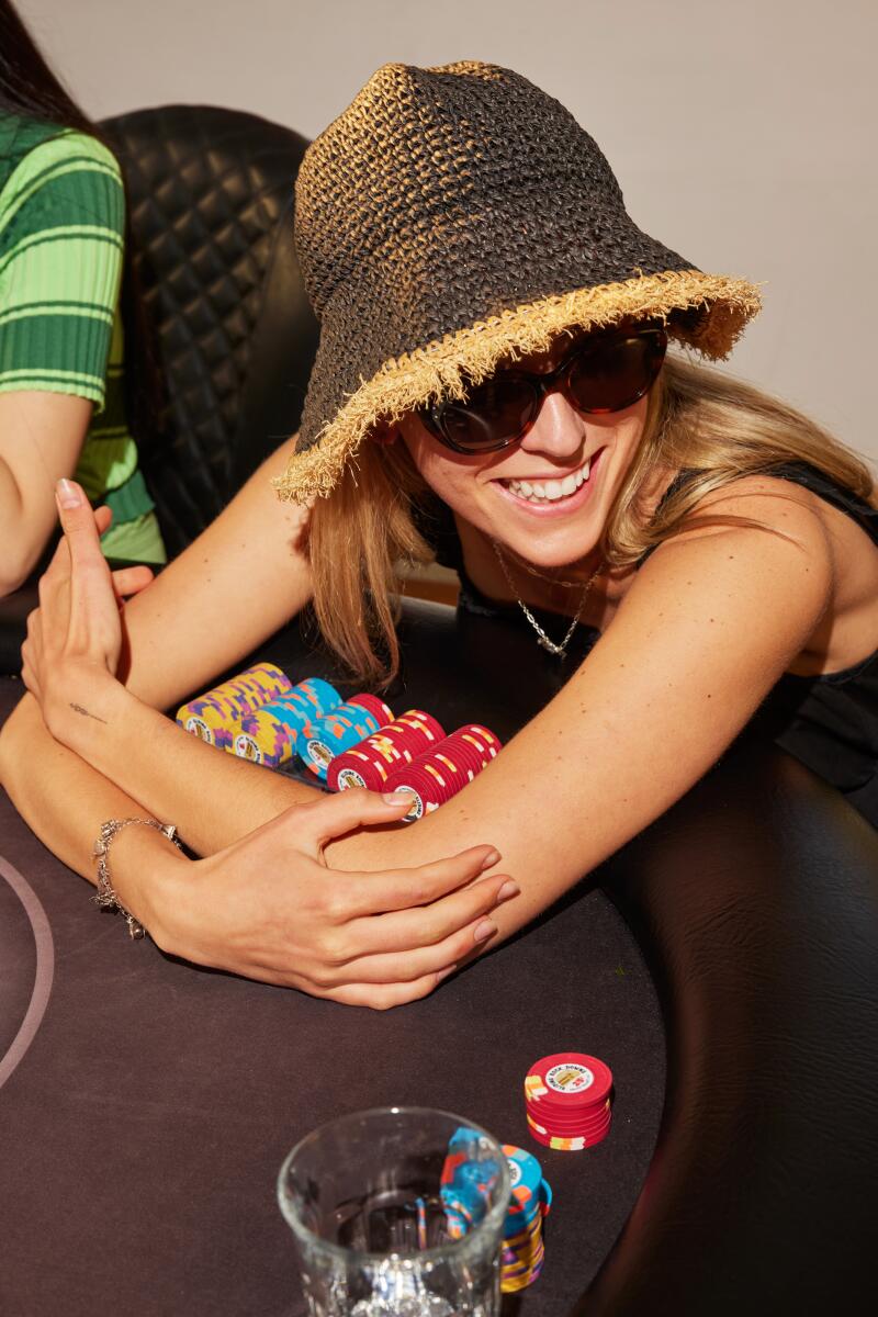 Artist Ava McDonough, wearing sunglasses and a straw hat, hugs her poker chips close.
