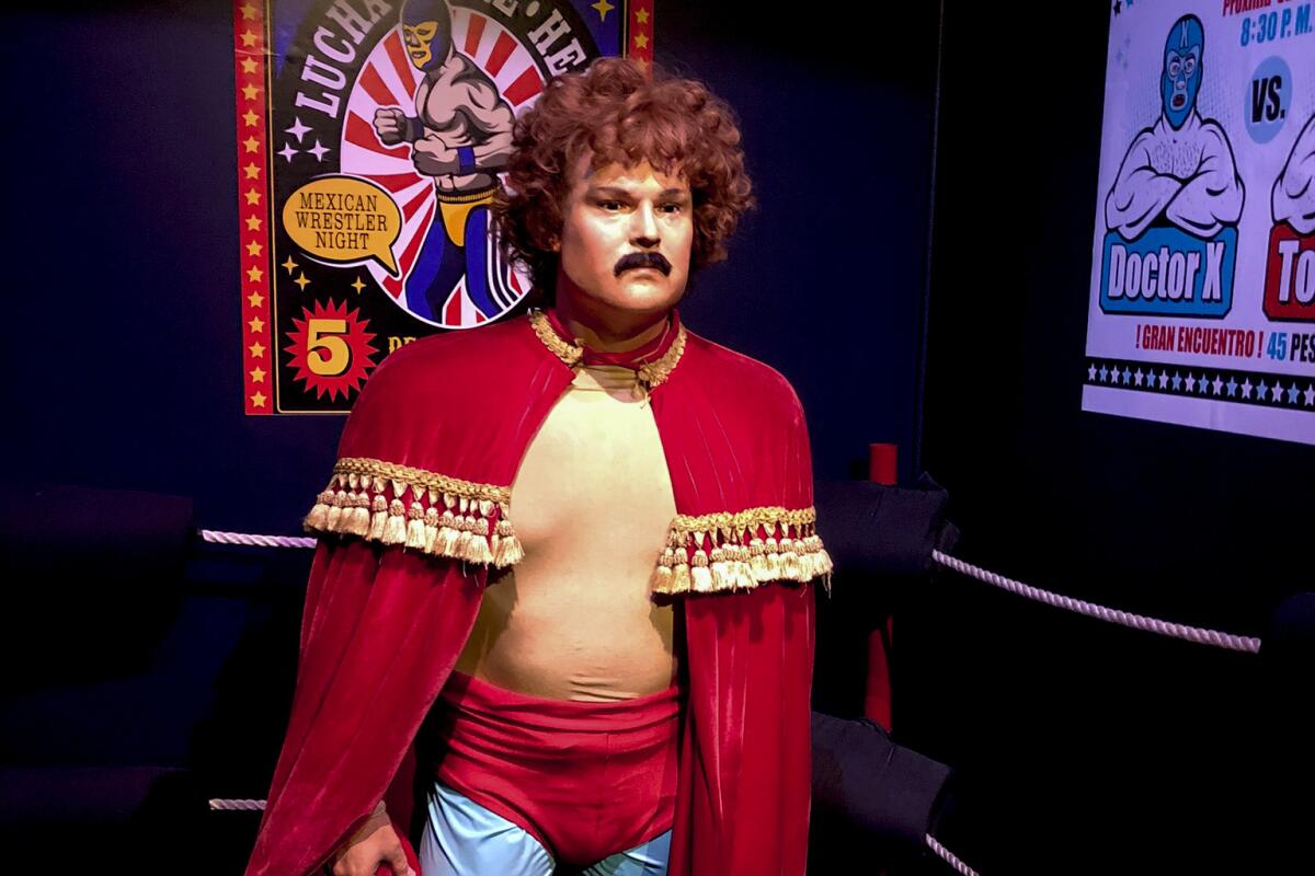 A wax figure of a mustachioed man in wrestling attire and a red cape