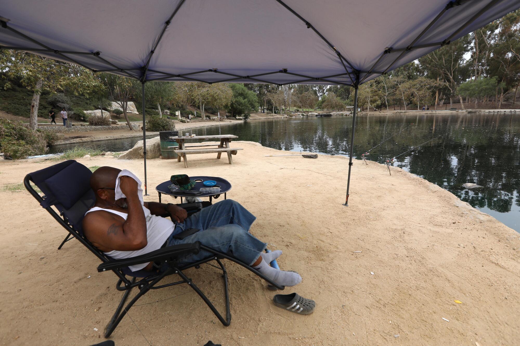 一名男子坐在湖边擦去脸上的汗水。