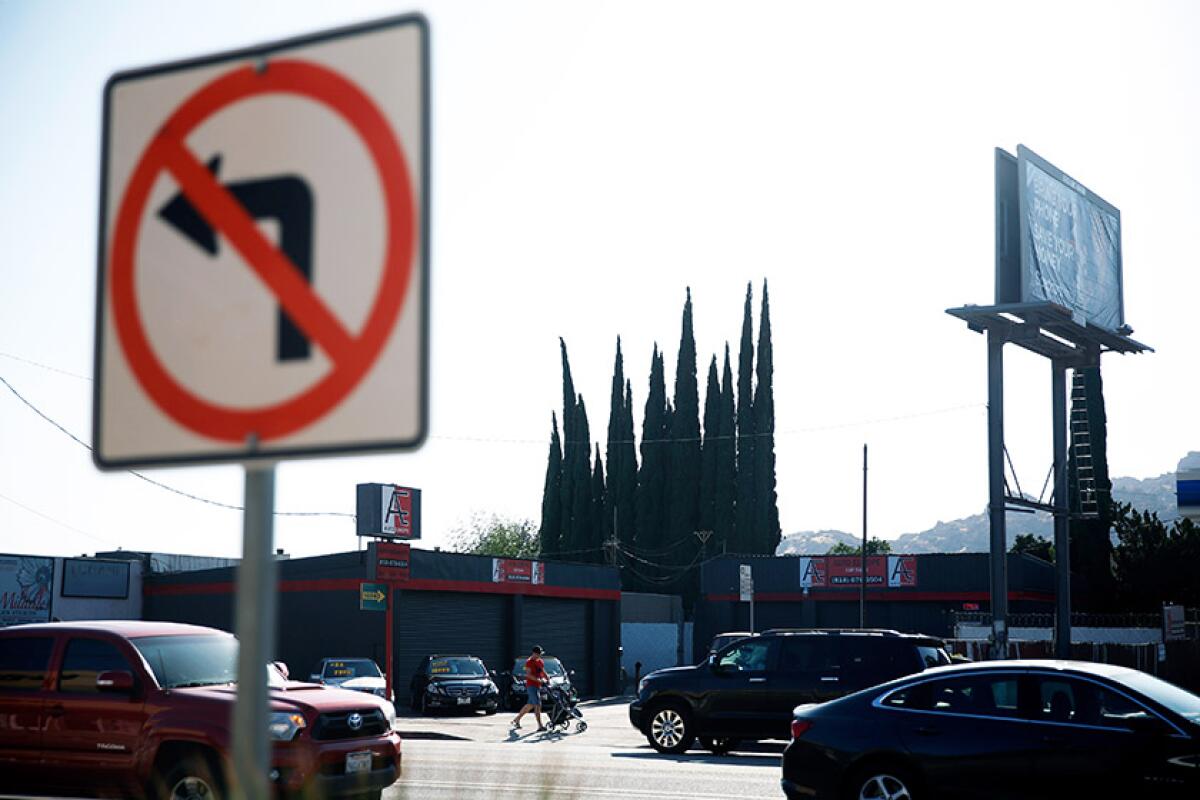 Cars drive by a street with a street sign in the foreground and business in the background