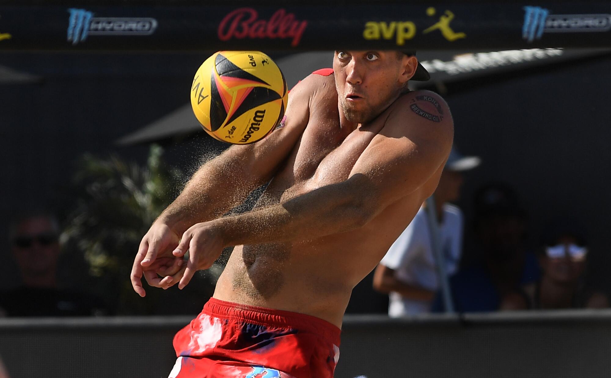 A man in red swim trunks hits a volleyball with both arms extended in front of him.