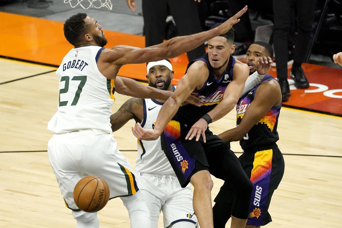 Phoenix Suns guard Devin Booker, right, dishes off around Utah Jazz center Rudy Gobert (27) during the first half of an NBA basketball game, Wednesday, April 7, 2021, in Phoenix. (AP Photo/Matt York)